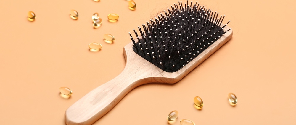 Brush with fallen down hair and pills on orange background