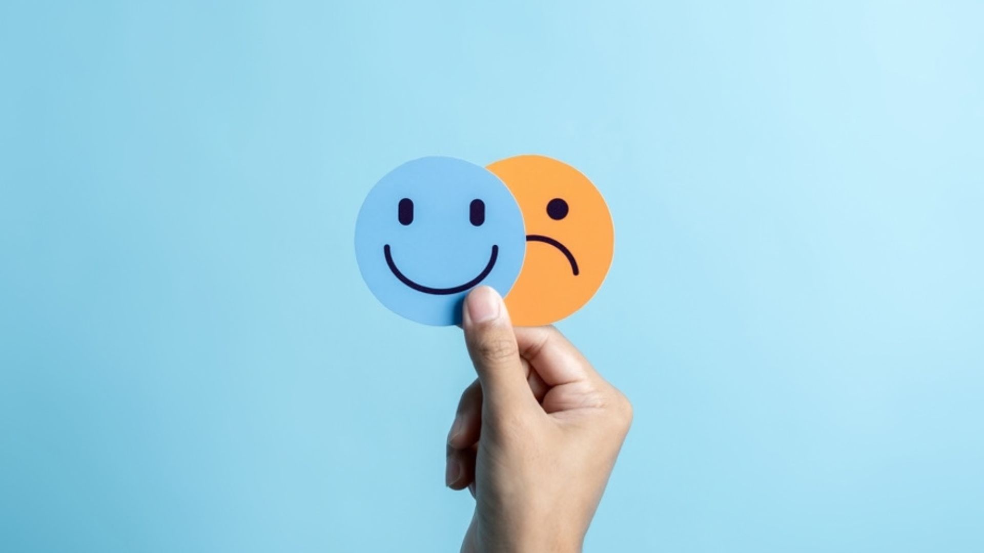 Hand holding smiley blue face and orange smiley face.