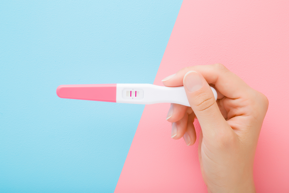 Pink and white pregnancy test against a blue and pink background.