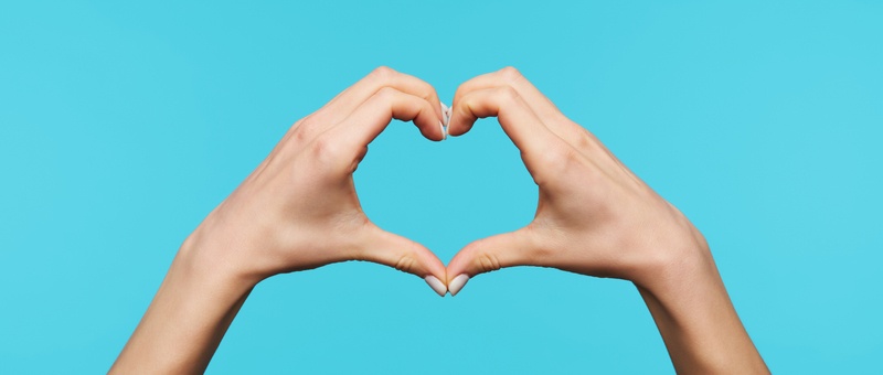 Female heart hands against blue background.