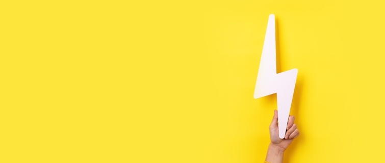 Hand holding white cut-out lightning bolt over yellow background.