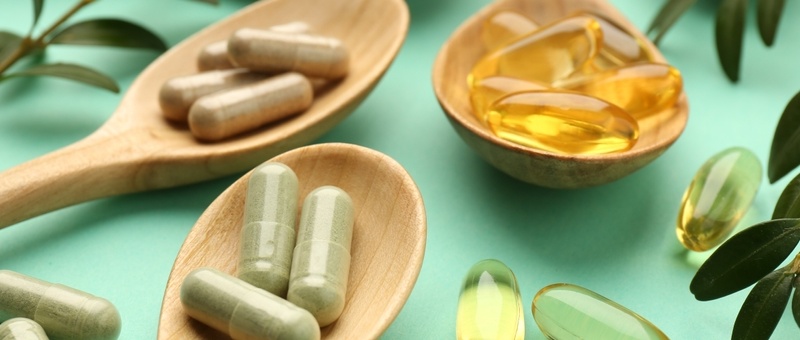 Wooden spoons against green background containing various supplement capsules.
