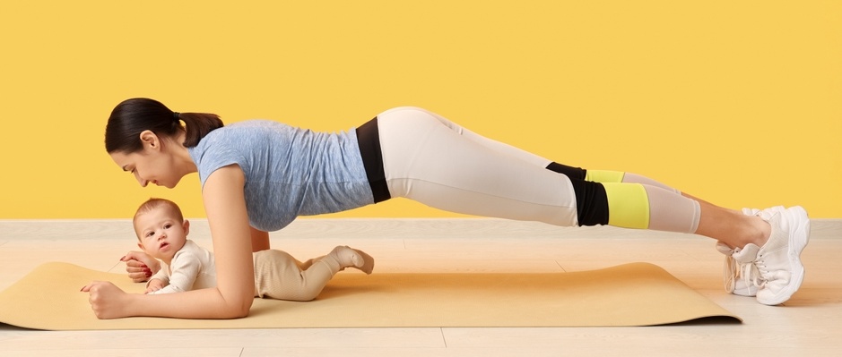 Beautiful young sporty woman with her little baby practicing yoga near yellow wall