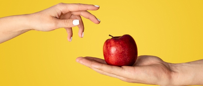 Man and woman with ripe red apple on orange background, close up of hands.