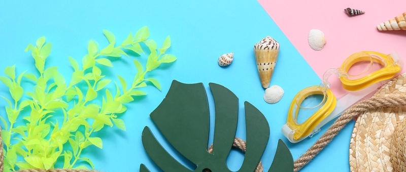 Wicker hat with swimming goggles, rope, seashells, leaf, and seaweed on bright pink and blue background.