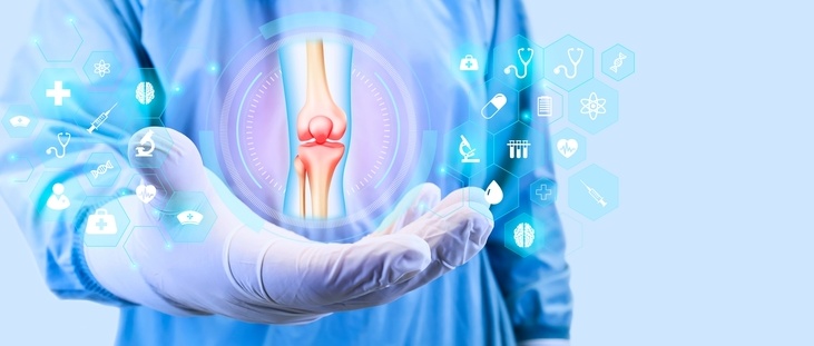 Doctor in blue scrubs and medical gloves with hand outstretched holding floating graphic of a knee scan surrounded by floating medical icons against a pale blue background.