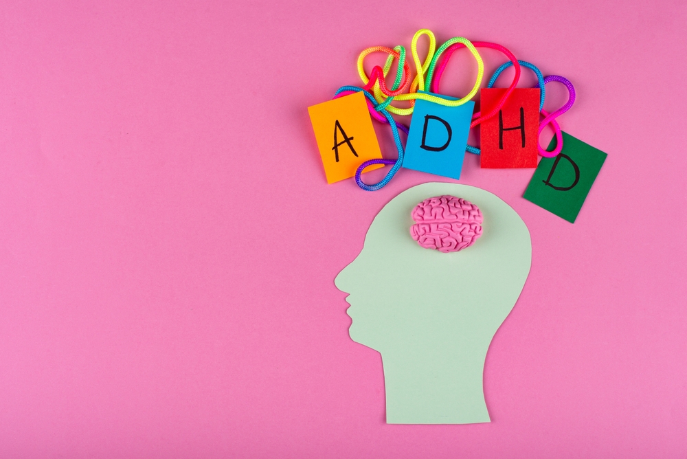 Paper silhouette of head with pink brain connected to colourful ADHD letters on pink background.