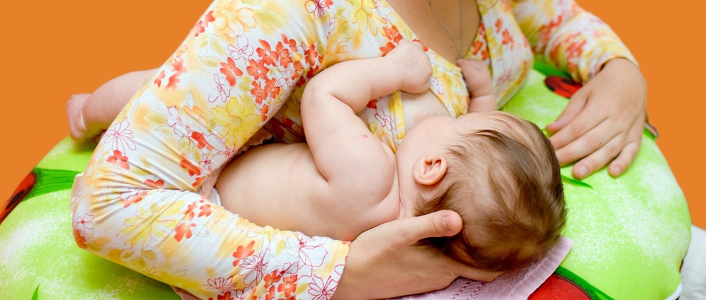Mother is breast-feeding a newborn baby. Isolated on orange background with clipping path