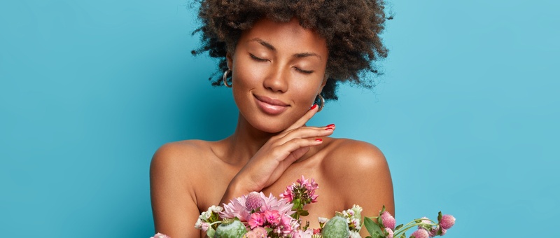 Bottom view of female face holding brightly coloured flowers against a blue background.