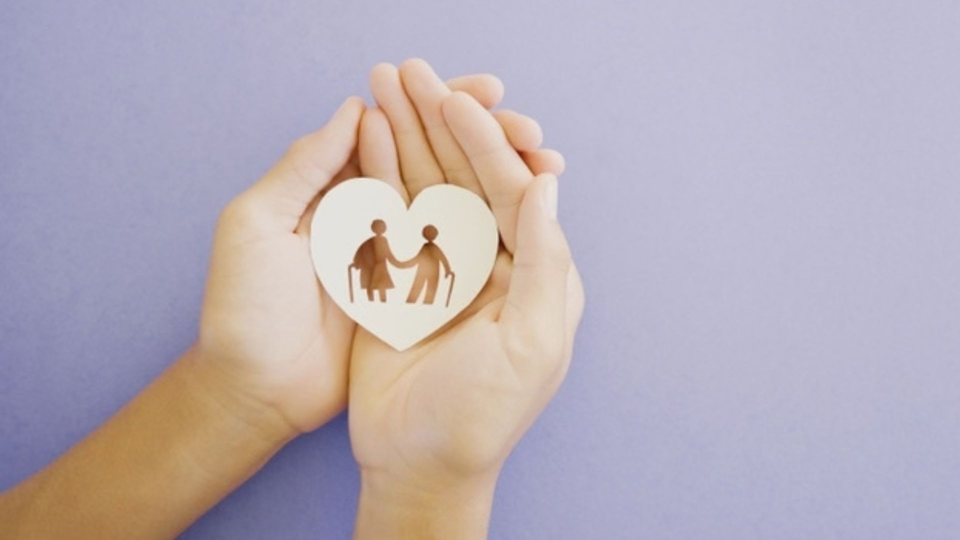Pair of hands holding paper heart with die-cut of elderly couple against a purple background.