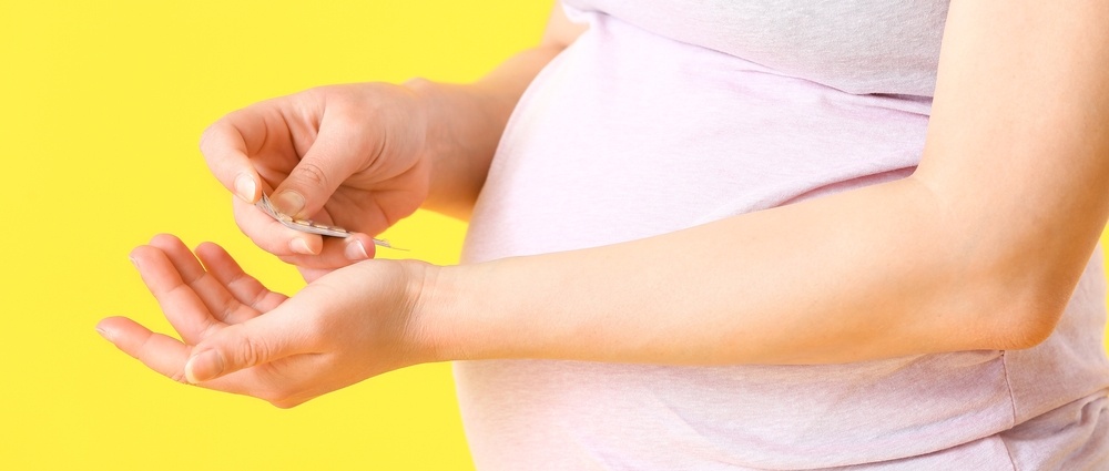 Young pregnant woman taking pills on color background, closeup