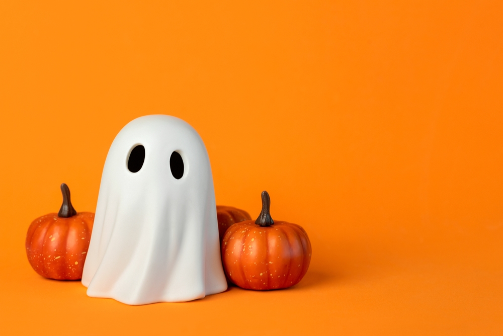 Funny Halloween ghost and Halloween pumpkins against orange background.
