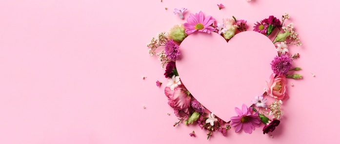 Pink heart on pink background surrounded by red, white and pink flowers.