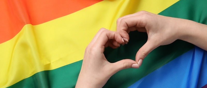 Woman making heart with her hands against rainbow LGBTQ+ flag.