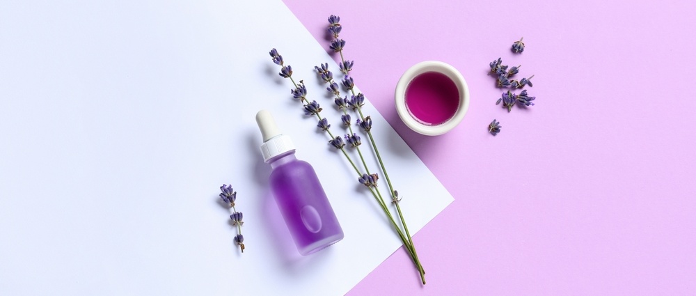 Flowers, bottle and bowl of lavender essential oil on colour background