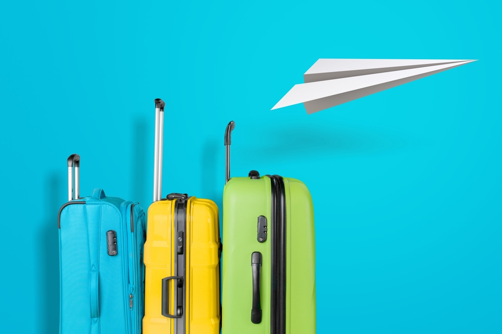 Blue, yellow, and green suitcases beneath paper aeroplane against blue background.