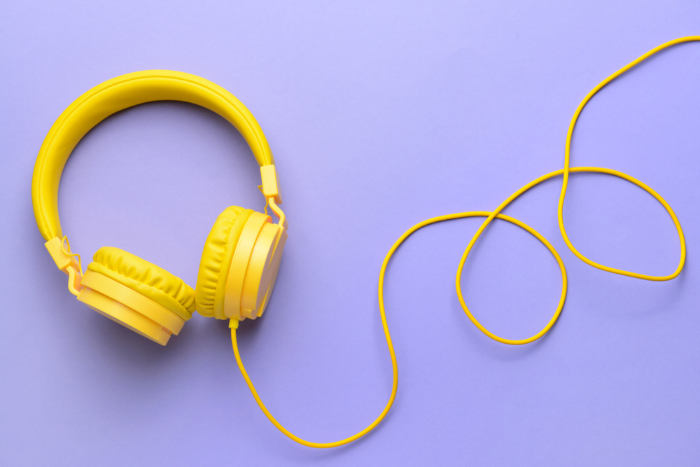 Yellow headphones with wire against purple background.