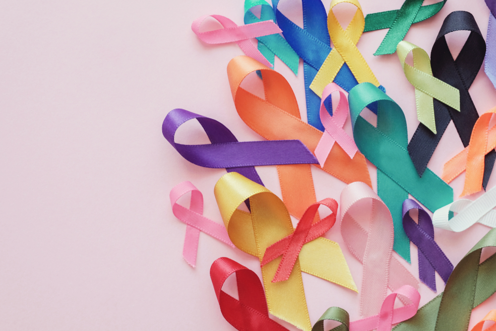 Colourful awareness ribbons in pink, blue, yellow, green, purple and orange scattered on a pink background.