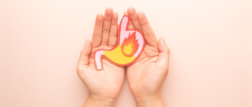 Human stomach burn with acid reflux and fire made from paper on hands. Gastroesophageal reflux disease (GERD) or heartburn symptoms. Gastrointestinal system disease and digestive problems.