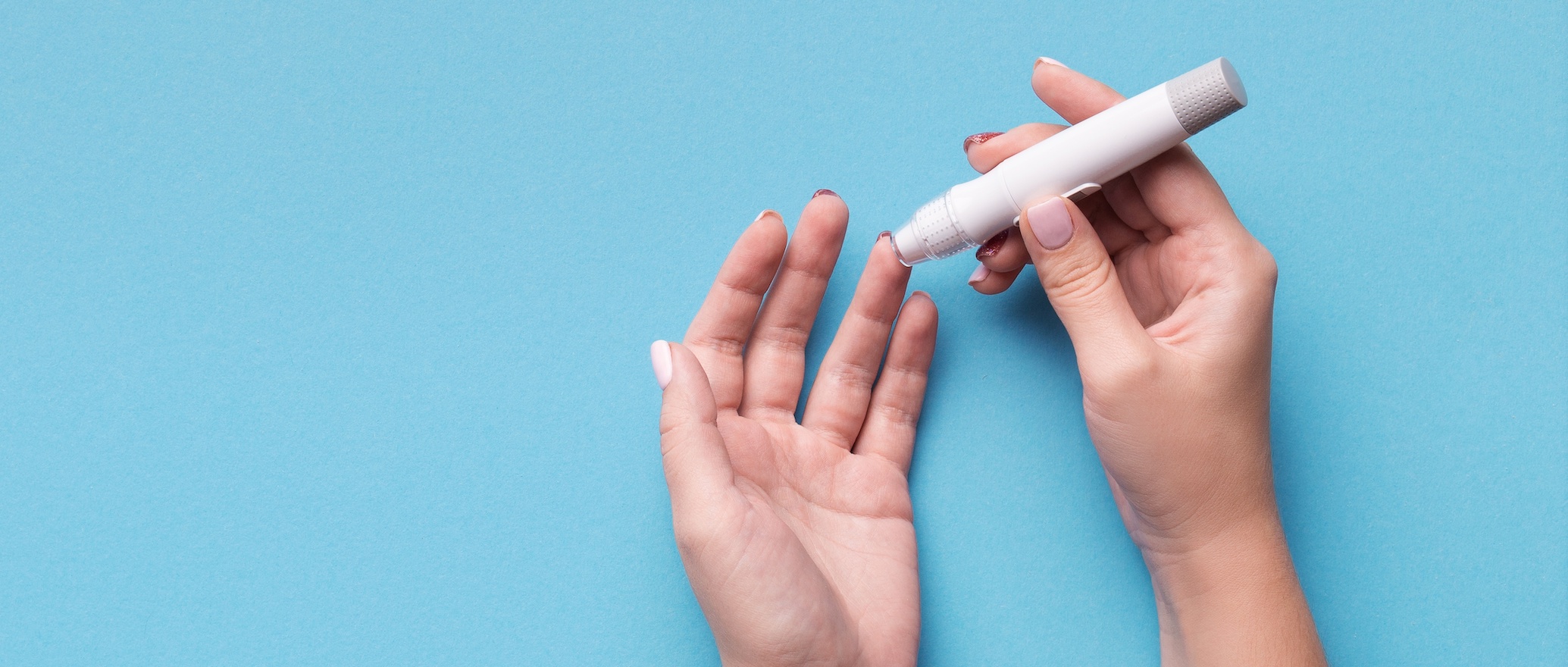 Hands holding a insulin pen against a light blue background.