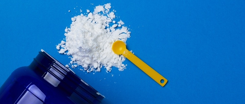 Close up of creatine powder and spoon on blue tile background