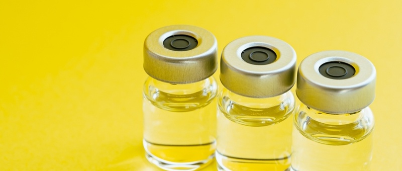 Line of glass vaccination bottles against yellow background.