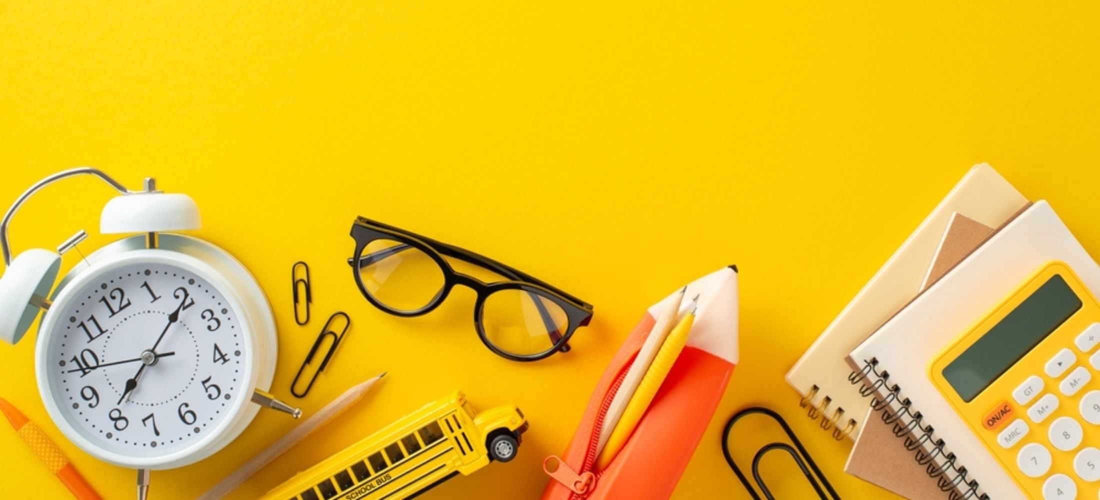 Back-to-school scene from top view, showcasing stationery, notebooks, pencil case, calculator, timer, glasses, car toy, clips. Vibrant yellow backdrop.