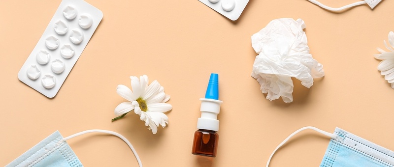 Nasal drops with medical masks, pills, flowers and tissues on beige background.