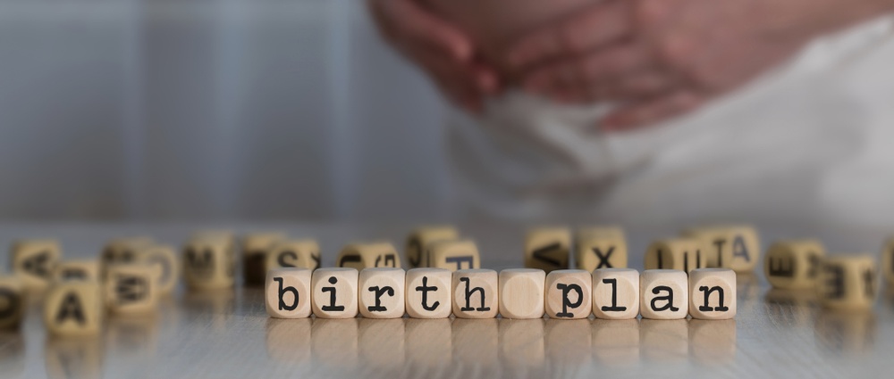 Words BIRTH PLAN composed of wooden letters. Pregnant woman in the background