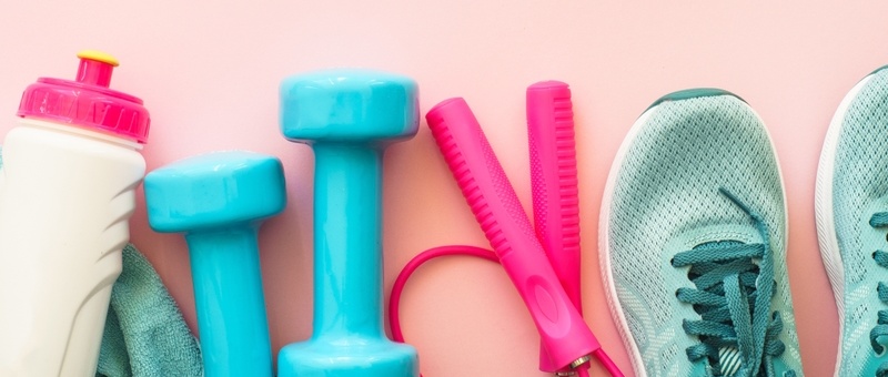 Cream, pink and yellow plastic water bottle, blue dumbbells, pink skipping rope and blue running shoes against a pale pink background.