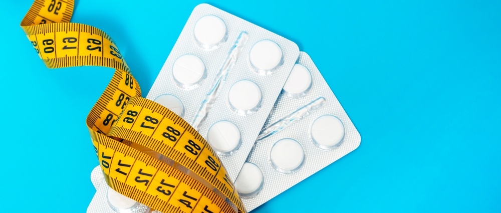 Two plates of tablets wrapped with a centimeter tape on a blue background close-up. The concept of weight loss, fat burner, vitamins, sports nutrition.