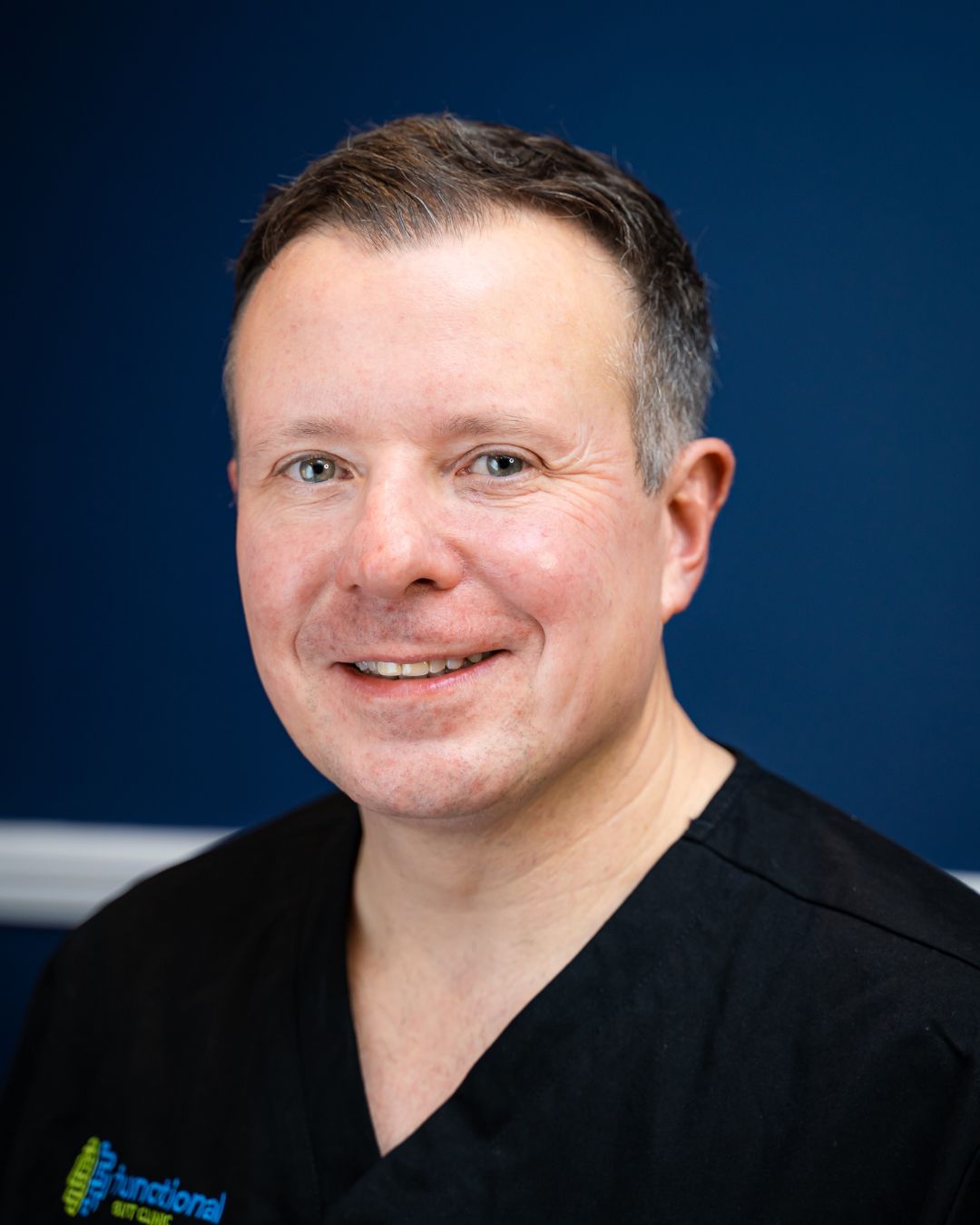 Professor Anthony Hobson of The Functional Gut Clinic, and host of The Functional Gut Diaries - white Caucasian male with short brown, grey hair in dark blue medical uniform against a dark blue background.