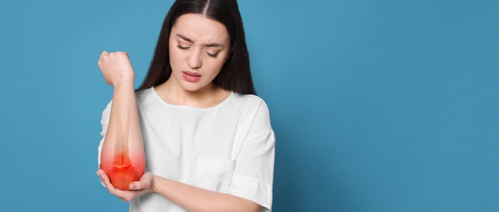 Arthritis symptoms. Young woman suffering from pain in elbow on light blue background, space for text