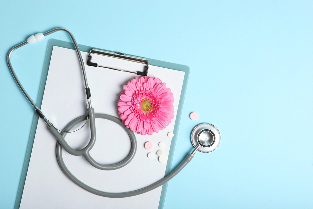 Medical clipboard beneath stethoscope and pink flower against a blue background.