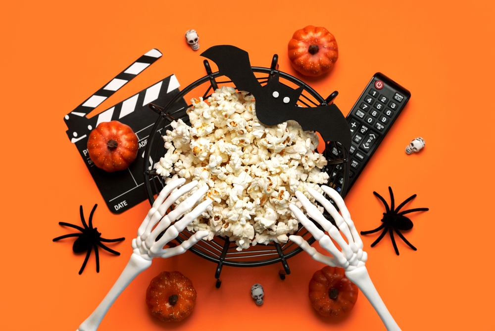 Halloween movies concept. Top view of bowl of popcorn, movie clapperboard, Halloween party decoration and television remote control over orange background.