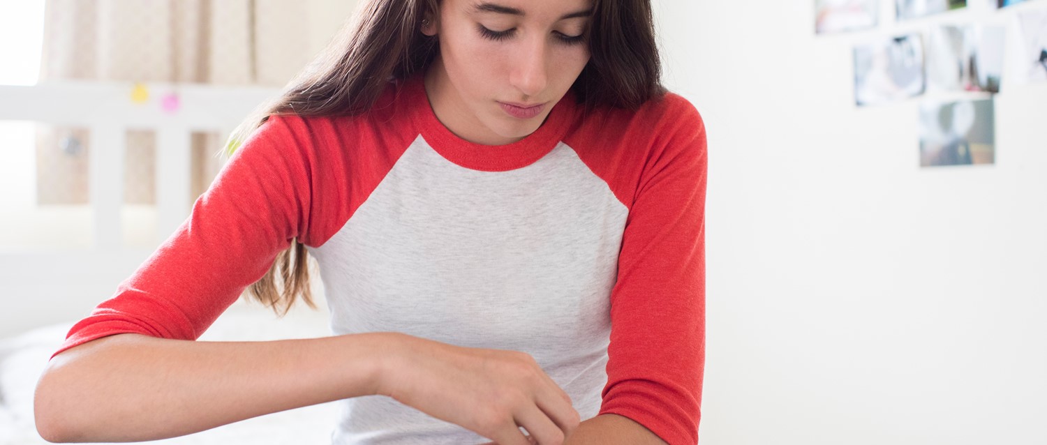 Person in red and white baseball-style shirt scratching her arm at a bright indoor workspace.