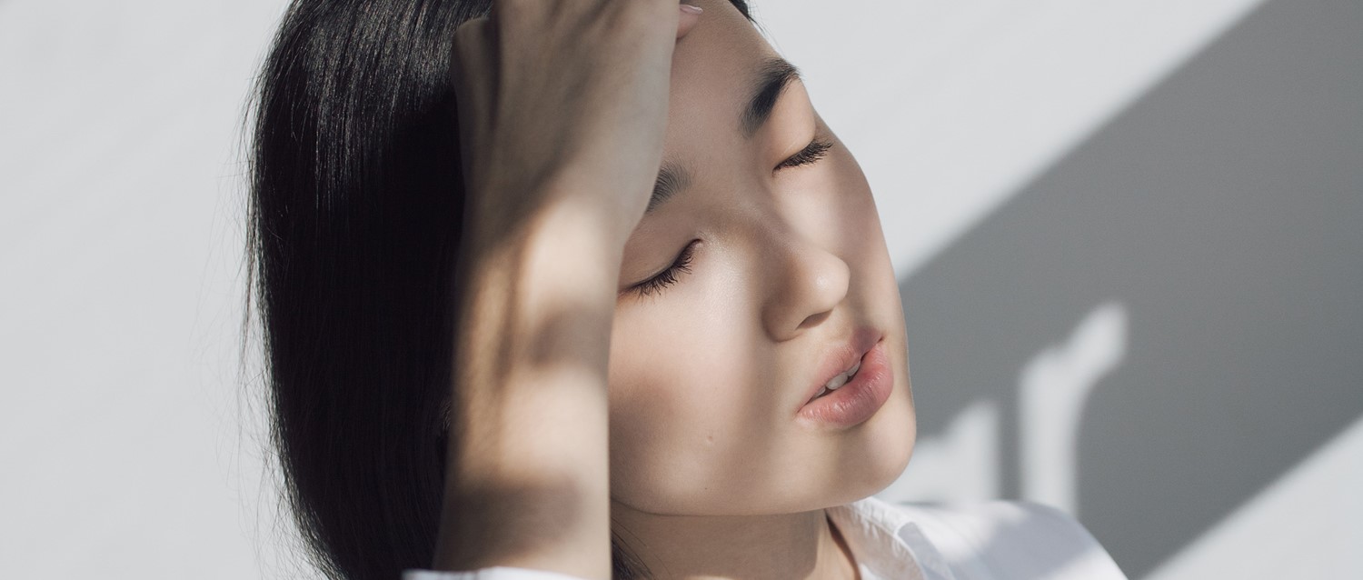 Person with dark hair and closed eyes in soft lighting, with shadows creating a serene, peaceful atmosphere.