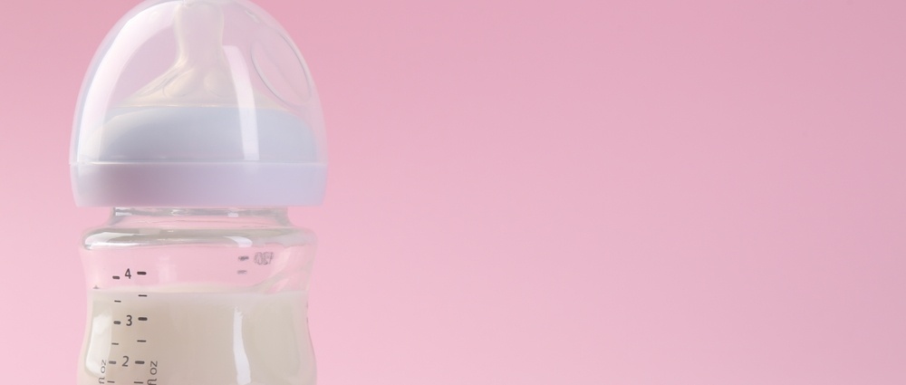 Feeding bottle with milk on pink background, space for text