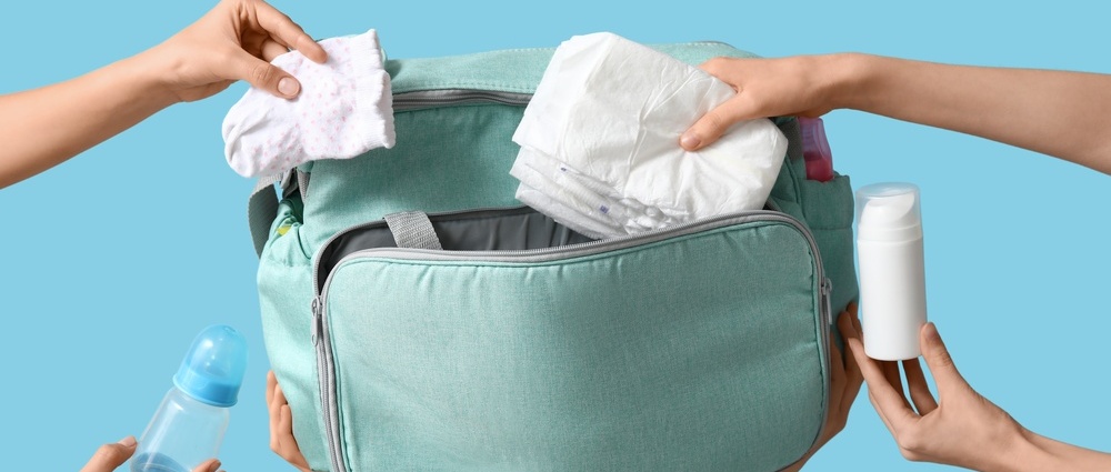 Many female hands with maternity hospital bag and baby things on blue background