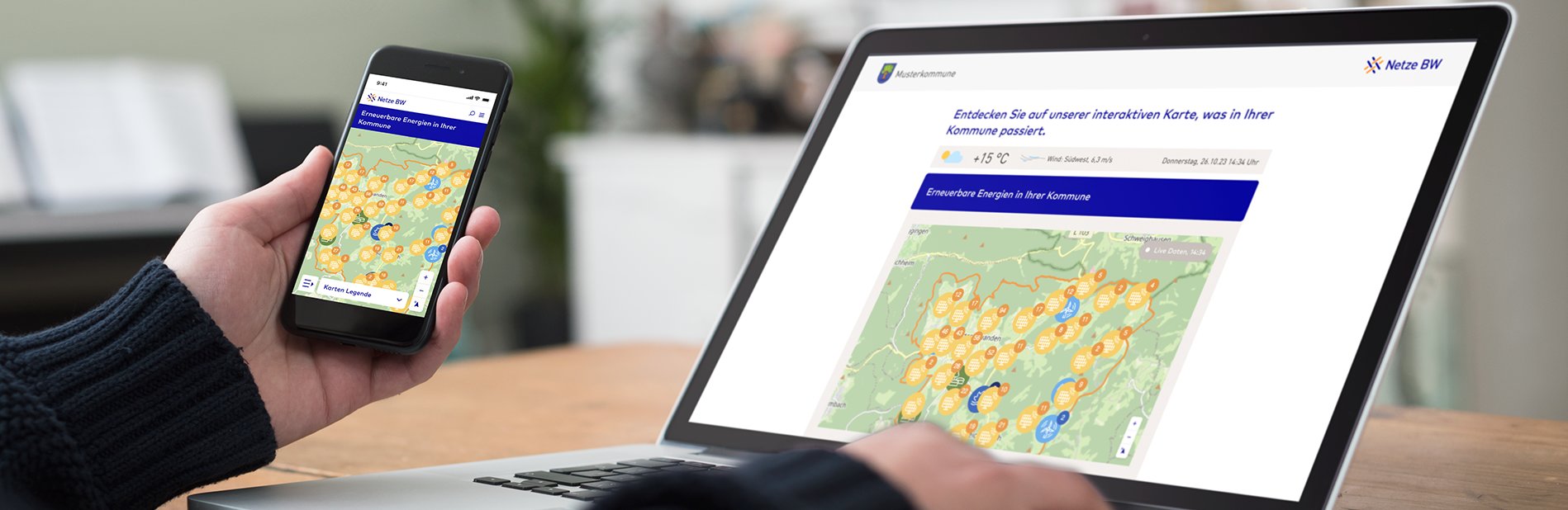 Eine Person sitzt am Laptop und hält ein Smartphone in der Hand. Es wird auf beiden Bildschirmen die Oberfläche des NETZMonitors einer Musterkommune angezeigt.