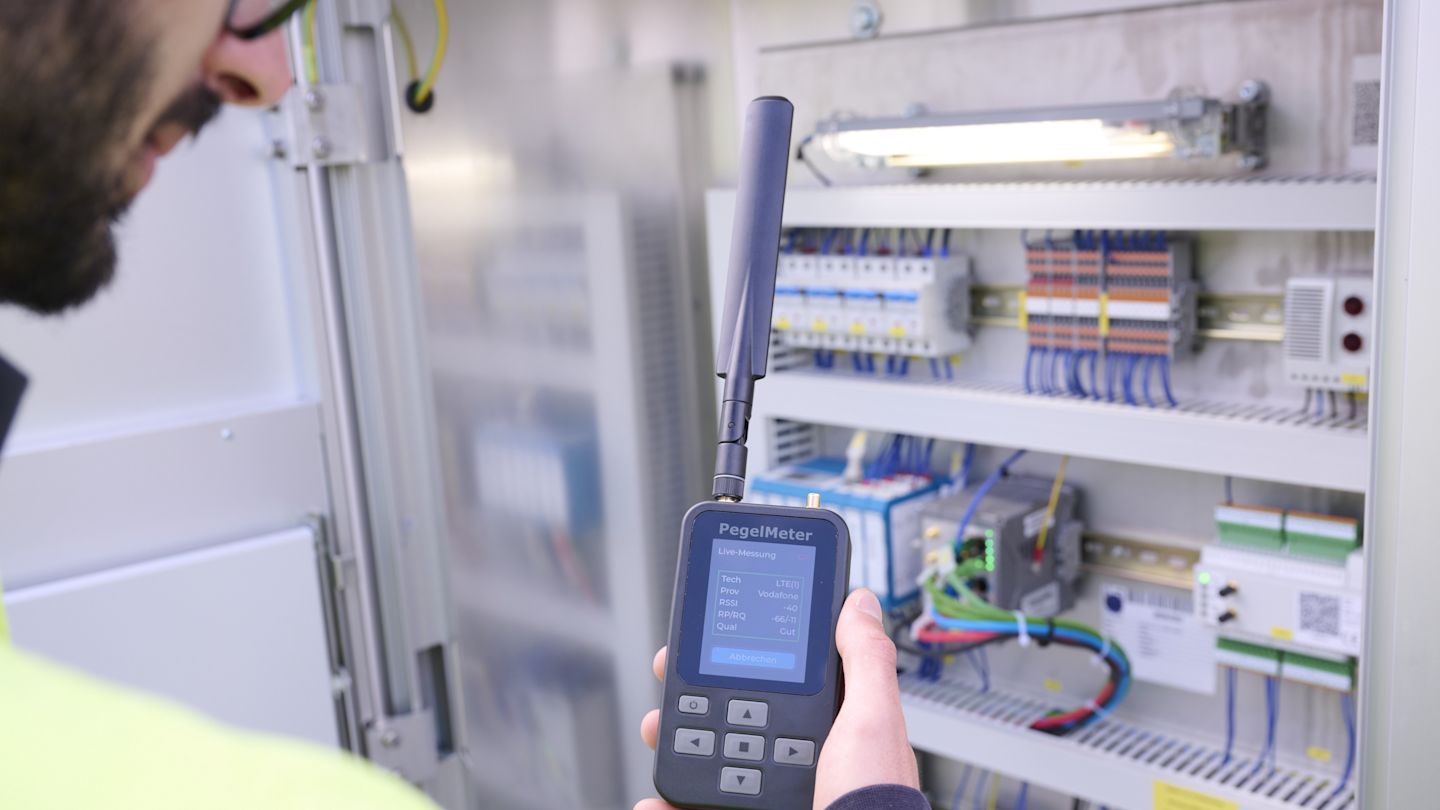 Ein Netze BW Mitarbeiter steht an einer Netzstation und misst mit einem PegelMeter den Mobilfunkempfang.