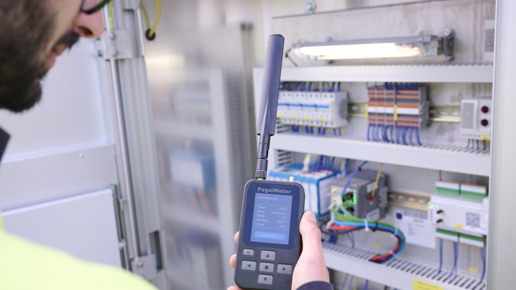 Ein Netze BW Mitarbeiter steht an einer Netzstation und misst mit einem PegelMeter den Mobilfunkempfang.