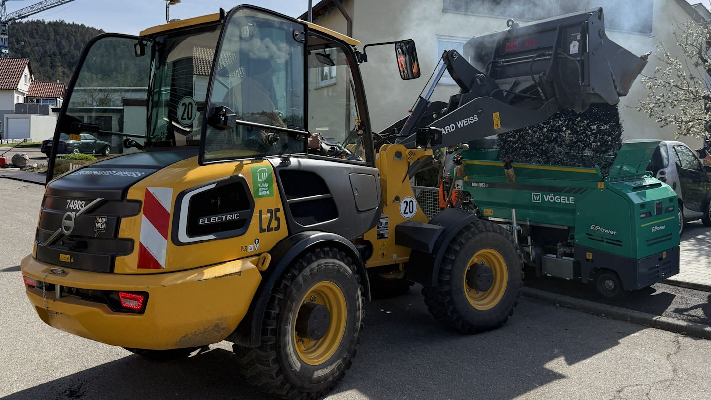 Elektrischer Frontlader beim Befüllen des elektrischen Gehwegfertiges mit Teer