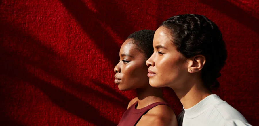 Two afro girls soaking up the sun in front of a red wall