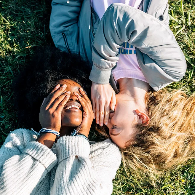 Two women laying on the grass with their faces covered.