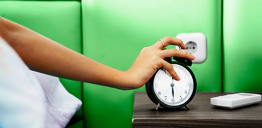 A woman's hand reaching for an alarm clock.