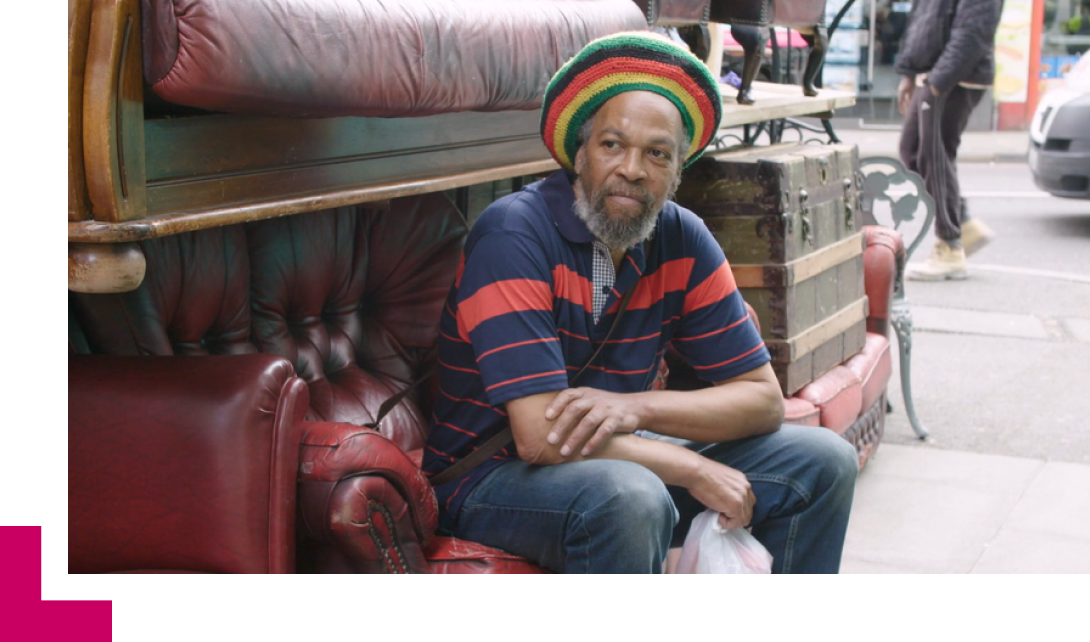 A Caribbean man sits on a sofa on the road and looks off-camera