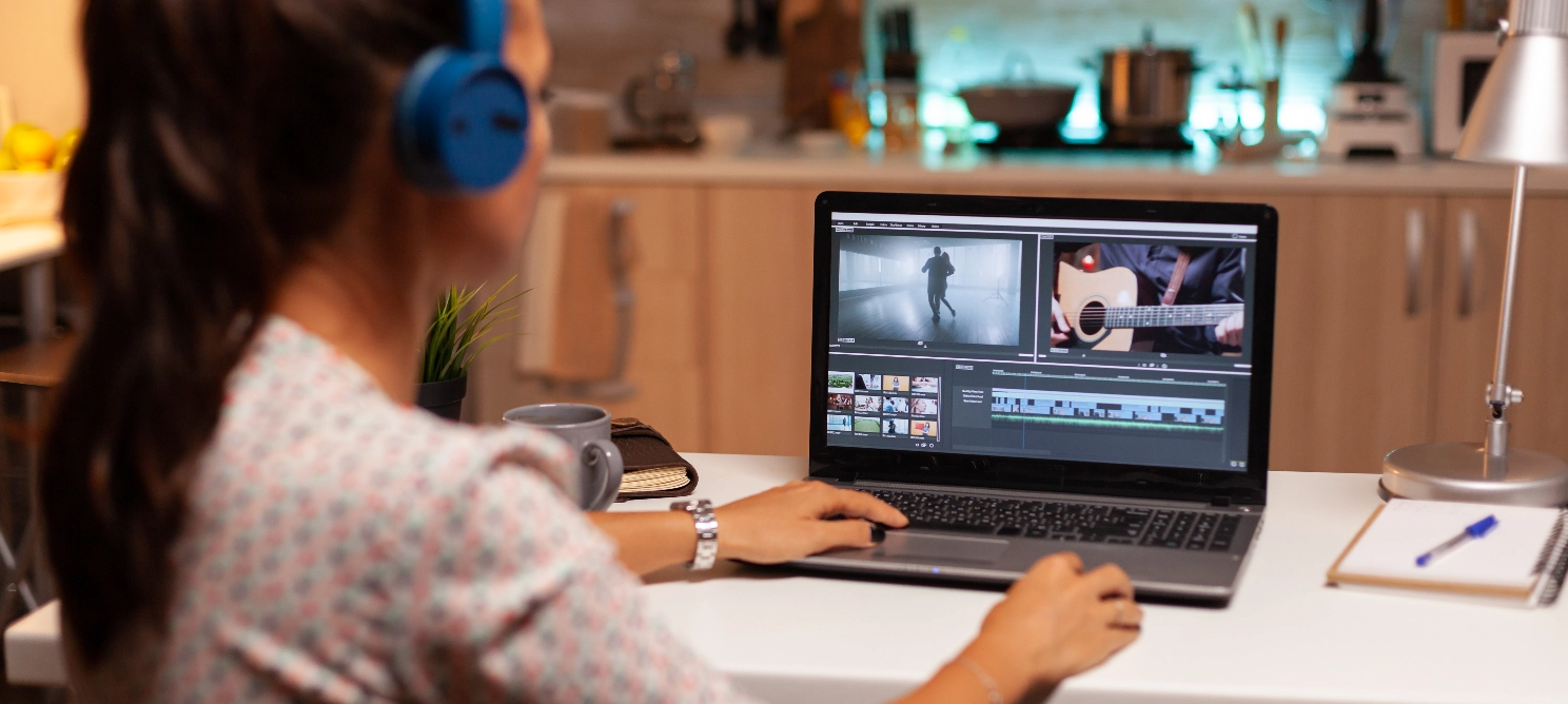 Person wearing blue headphones working on video content editing on a laptop in a kitchen setting, emphasizing the importance of quality content for SEO