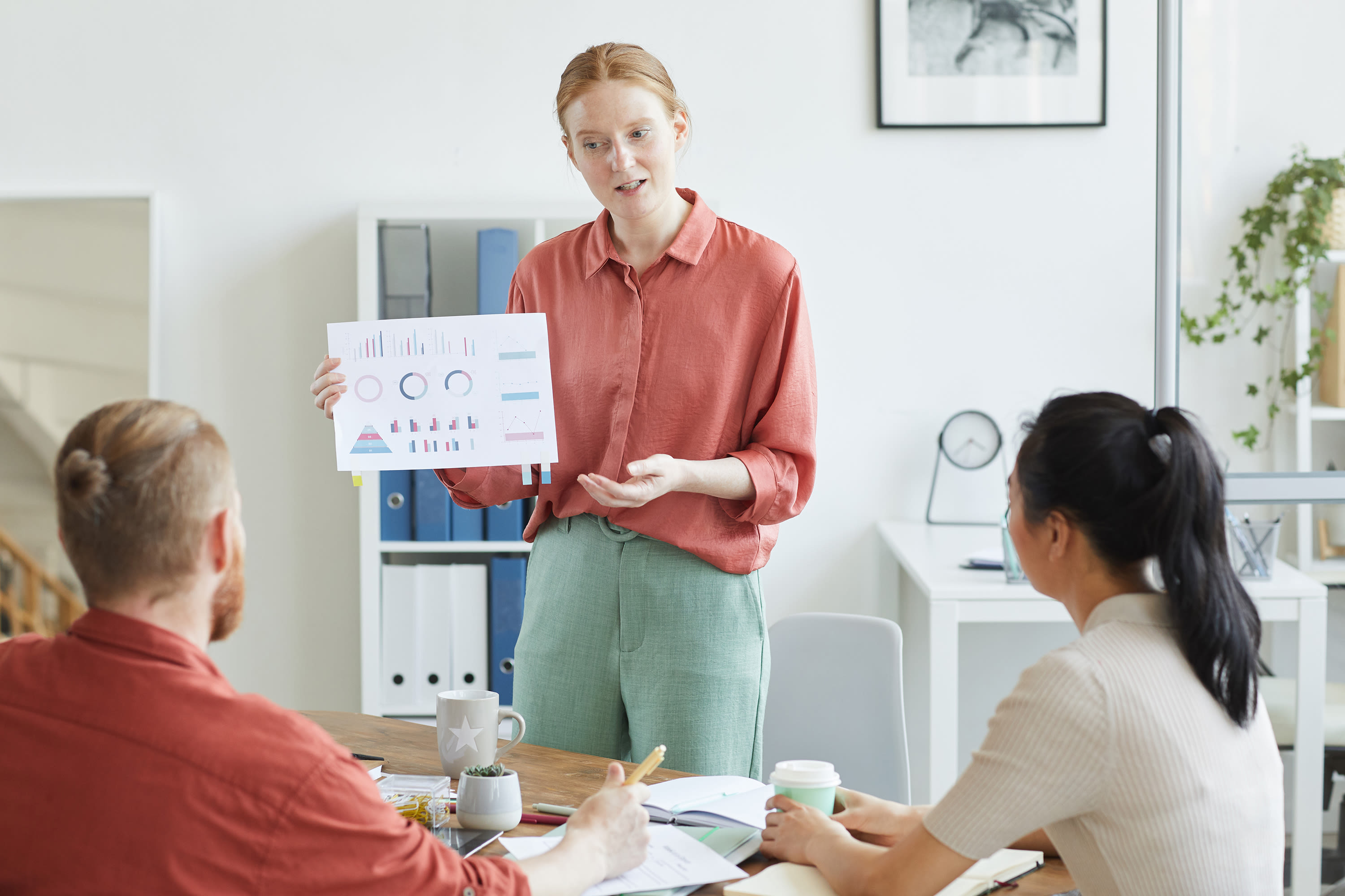 young-businesswoman-pointing-business-charts-her-hands-she-giving-business-presentation-her-colleagues-office2