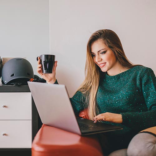 Mujer lee en su computador, mientras toma un café, sobre cómo retirar sus cesantías en el portal web de Protección